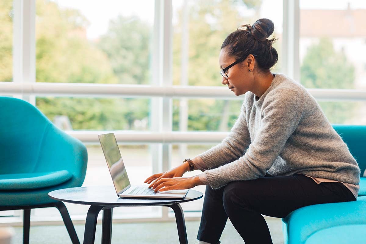 Dame sitter på en blå sofa og jobber på en laptop, til illustrasjon for sikker netthandel