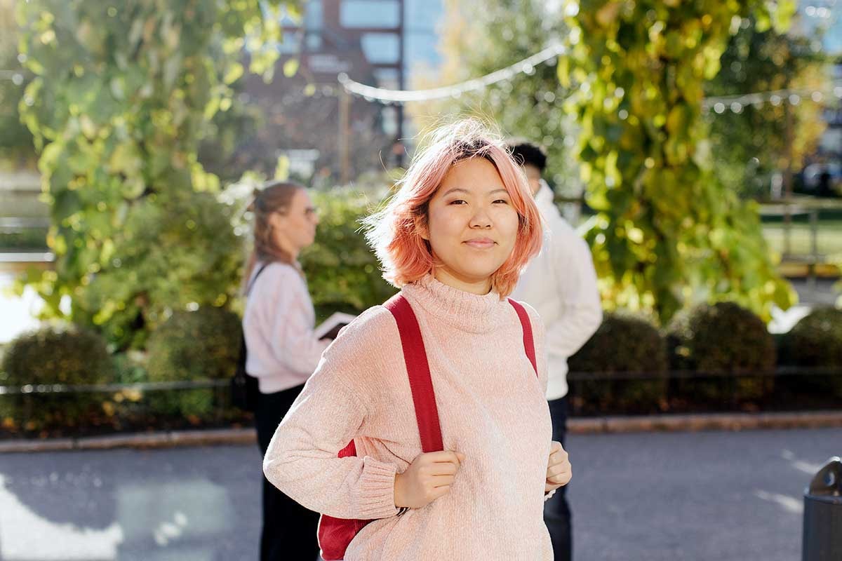 Jente med rosa hår står ute med en rød skolesekk, til illustrasjon for studentbudsjett