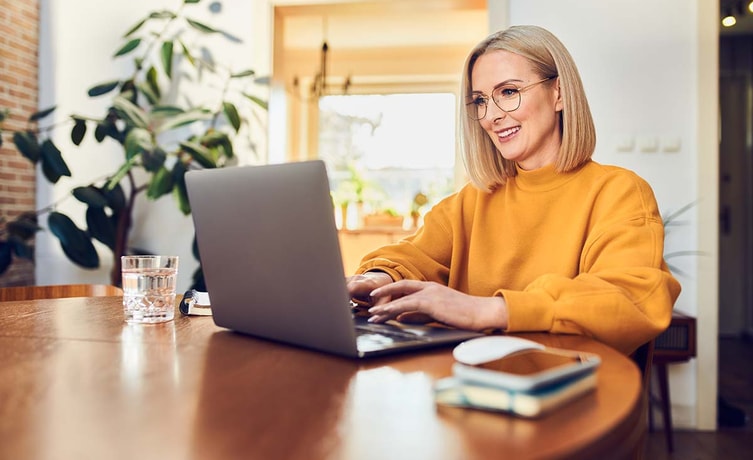 Dame i oransje grenser sitter ved spisebord og ser på datamaskin, til illustrasjon for betale til utlandet