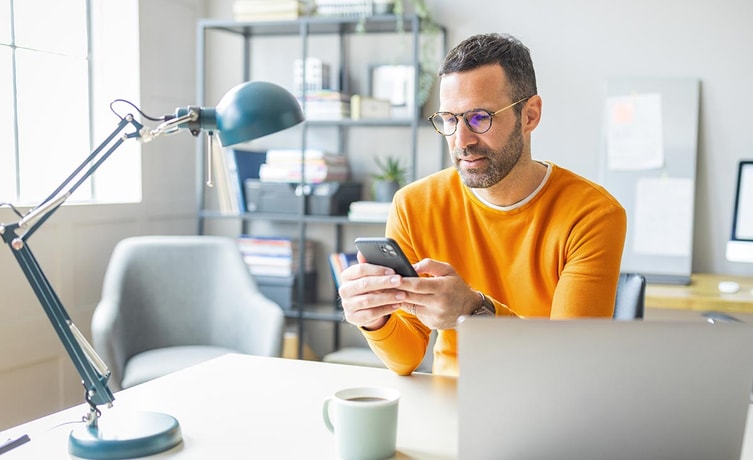 Mann i orange genser ser på mobilen, til illustrasjon for mine kort app