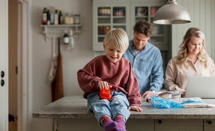Gutt på kjøkkenbenk, leker med en bil mens foreldrene står bak, til illustrasjon for familieøkonomi