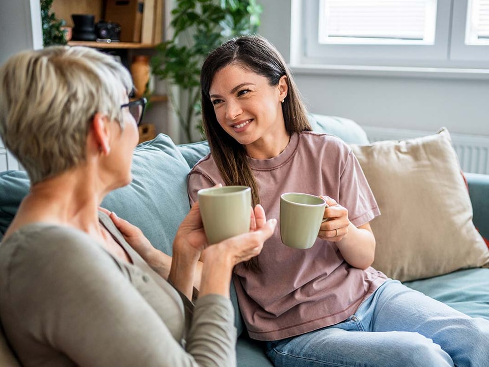 To kvinner sitter i en sofa og drikker kaffe, i forbindelse med hvordan hjelpe barna inn på boligmarkedet