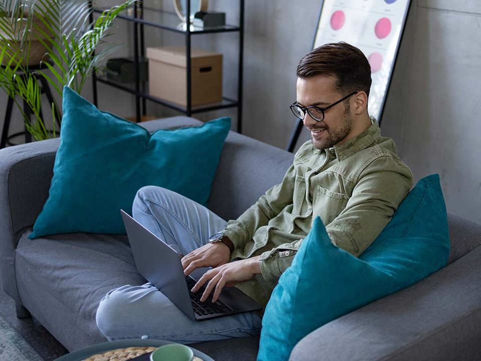 Mann sitter i en sofa og jobber på en PC, til illustrasjon for AvtaleGiro