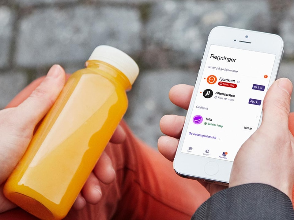 Mann sitter med en appelsinjuice i hånda og mobilen i den andre som du kan bruke til å betale regninger