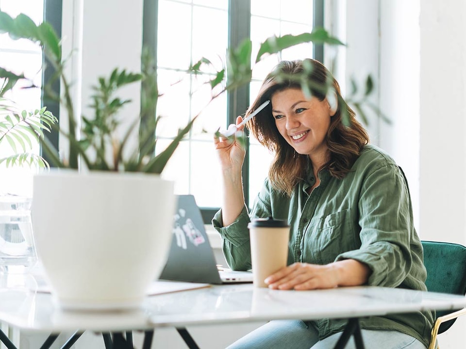 Smilende dame med kaffe ser på laptop, illustrasjon til veileder om hvordan hvordan signere dokumenter